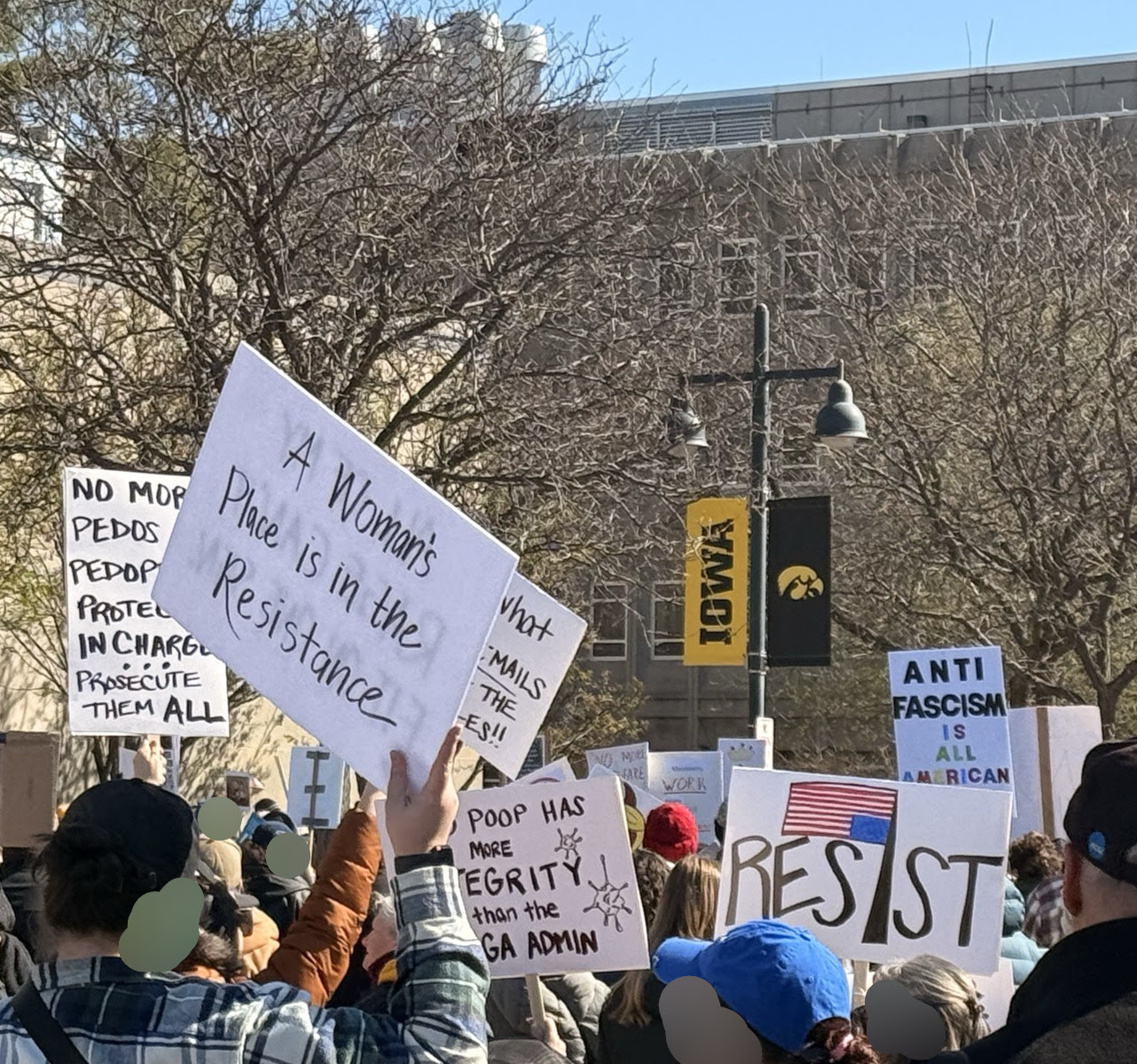 A closer image of some signs. Prominently featured text reads &lsquo;A woman&rsquo;s place is in the resistance&rsquo;, &lsquo;Resist&rsquo;, and &lsquo;Anti fascism is all american&rsquo;. Visible faces have been blurred for privacy.