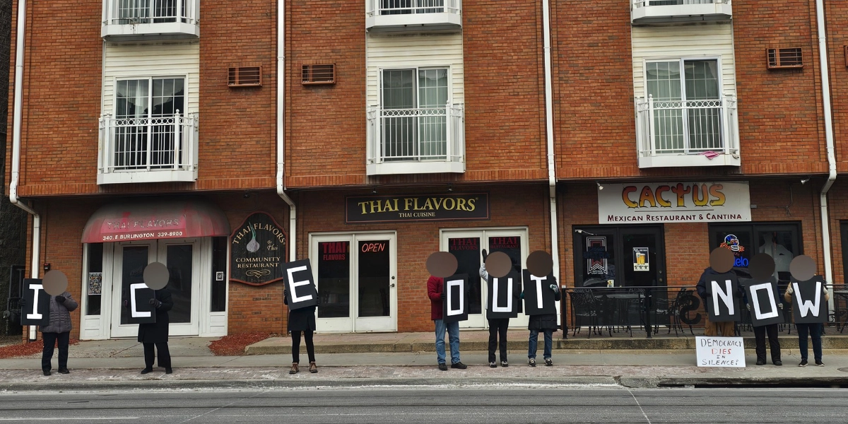 Volunteers holding letters spelling ICE OUT NOW on a sidewalk in downtown Iowa City
